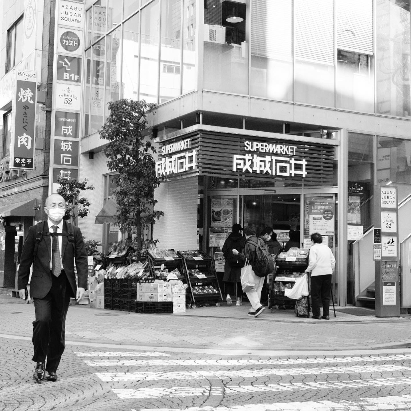 東京・麻布十番のスーパーの店先。買い物客が行き交う街並みのモノクロ写真
